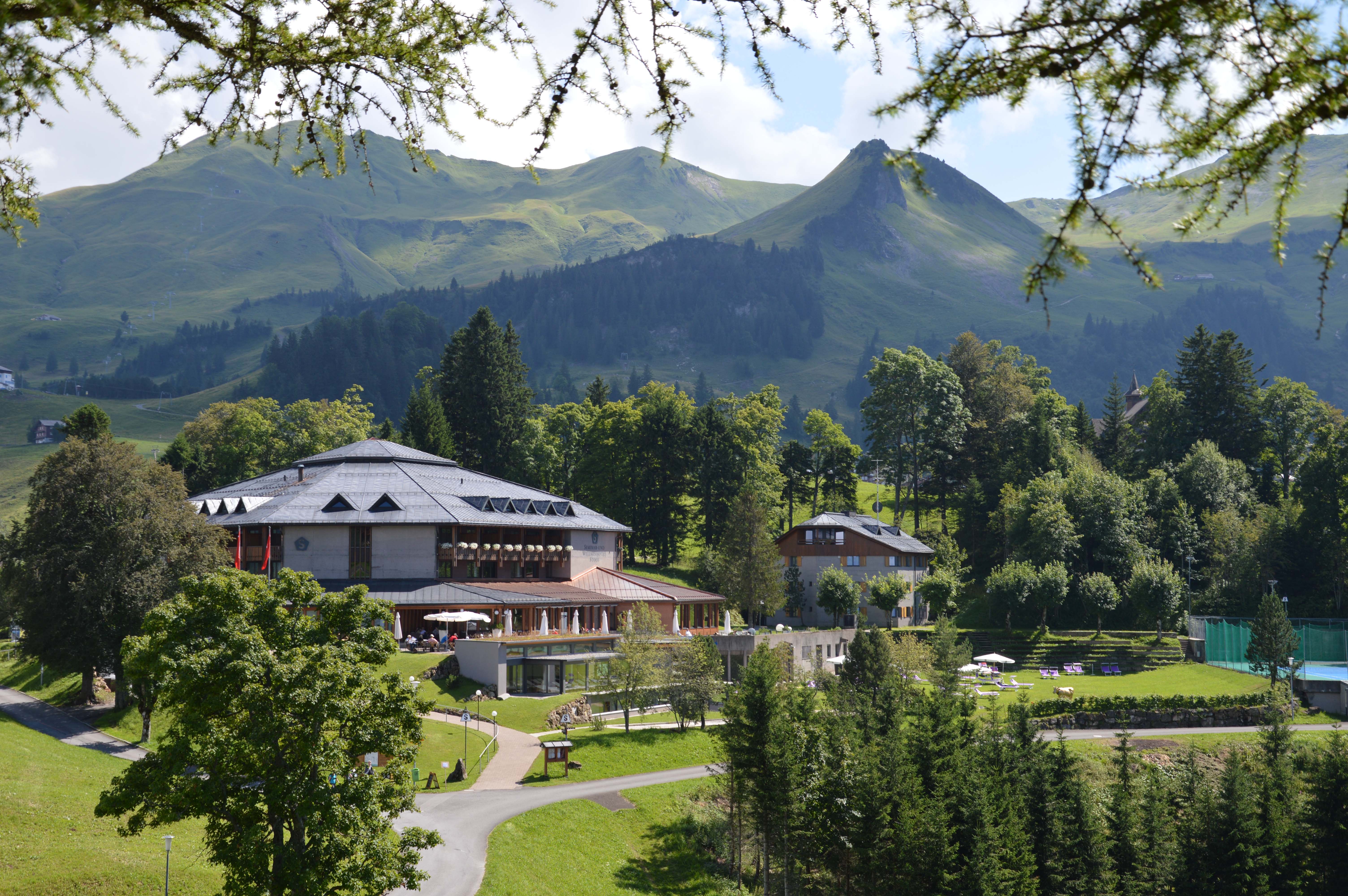 Hotel in grüner Parkanlage mit Teich und Blick auf die umliegenden Berge.